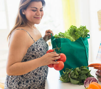 Woman unpacking fruits and vegetables from a shopping bag sitting on a kitchen counter