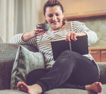 Woman holding a cup of tea while reading a book on a couch