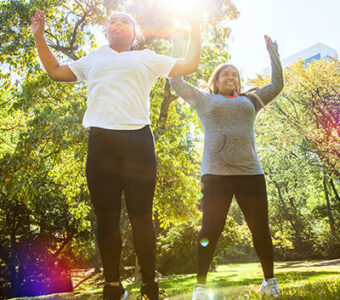 Mother and daughter doing jumping jacks and exercising outside in sun