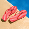 Red and white striped flip flop sandals sitting next to pool