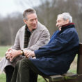 Elder parent laughing with middle aged adult on bench in park