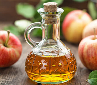 Small bottle of apple cider vinegar surrounded by apples