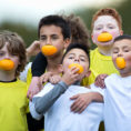 Group of young children holding each other and smiling with orange slices in their mouths