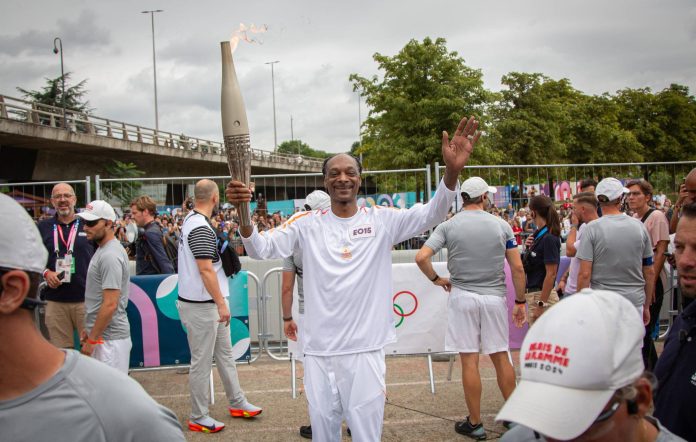 Rapper Snoop Dog carries the Olympic flame during the last stage of the Olympic torch before the Olympic Games 2024 opening ceremony in Seine-Saint-Denis, France on July 26, 2024 (Photo by Victoria Valdivia / Hans Lucas / Hans Lucas via AFP) (Photo by VICTORIA VALDIVIA/Hans Lucas/AFP via Getty Images)