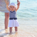 Infant walking with adult help on a beach near a body of water