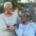 Woman standing with hands on the shoulder of a man in a wheelchair