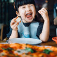 Young child laughing and eating pizza at a restaurant