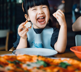 Young child laughing and eating pizza at a restaurant