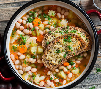 Pot full of vegetable soup with pieces of bread on top