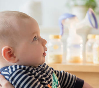 Person holding infant with bottles of milk and breast pump sitting in background