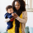 Woman holding baby while texting on mobile phone