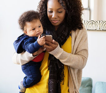 Woman holding baby while texting on mobile phone