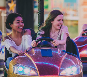 Two laughing young adults in a bumper car with another group in the background