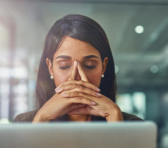 Person looking stressed and tired with hands at temple in front of computer