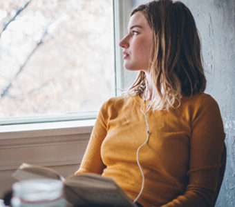 Woman wearing headphones and looking sadly out a window